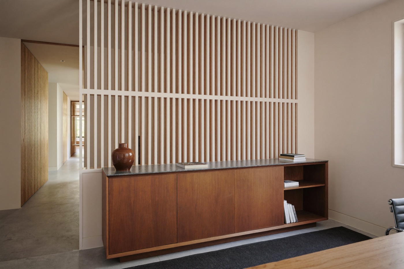 Low dark wood credenza with flush doors and a dark top, in front of a full-height partition of pale wood slats.