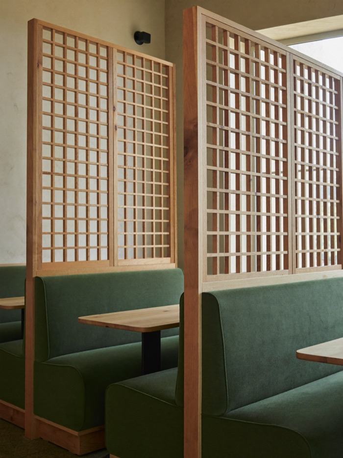 Restaurant booths in green upholstery separated by tall pale wood lattice screens.