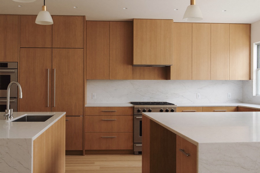 Kitchen with flat-panel light wood cabinets, a paneled refrigerator, white counters and two islands.