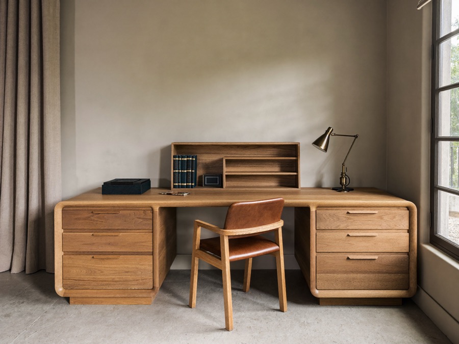 Warm wood desk with rounded edges and two drawer pedestals, a small shelf unit on top, in a grey-walled study.