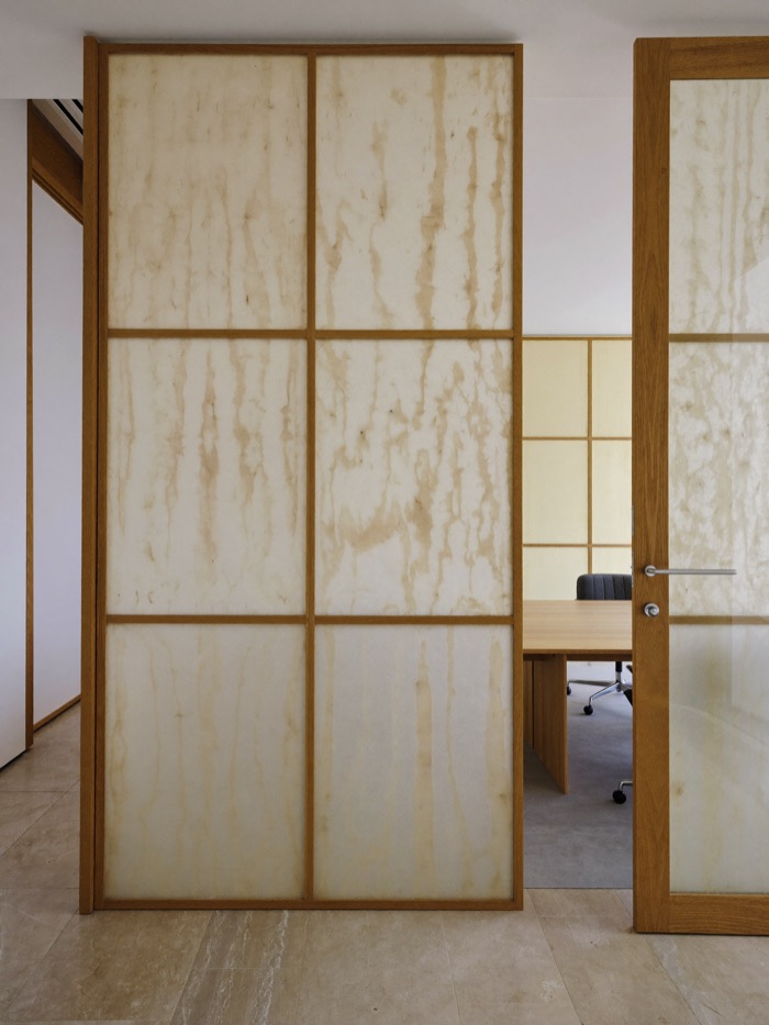 Meeting room partition of translucent panels in pale wood frames, with a conference table visible through the open door.
