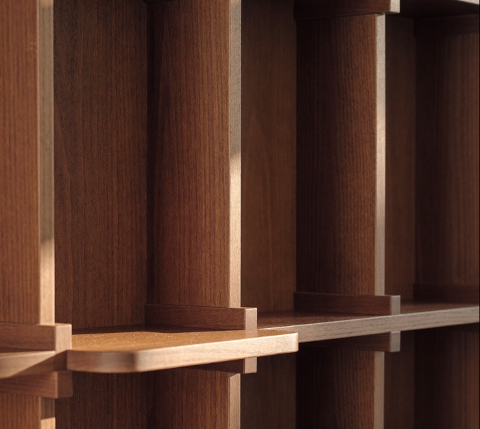 Close view of wood shelves set into vertical wood uprights, lit by low raking sun.