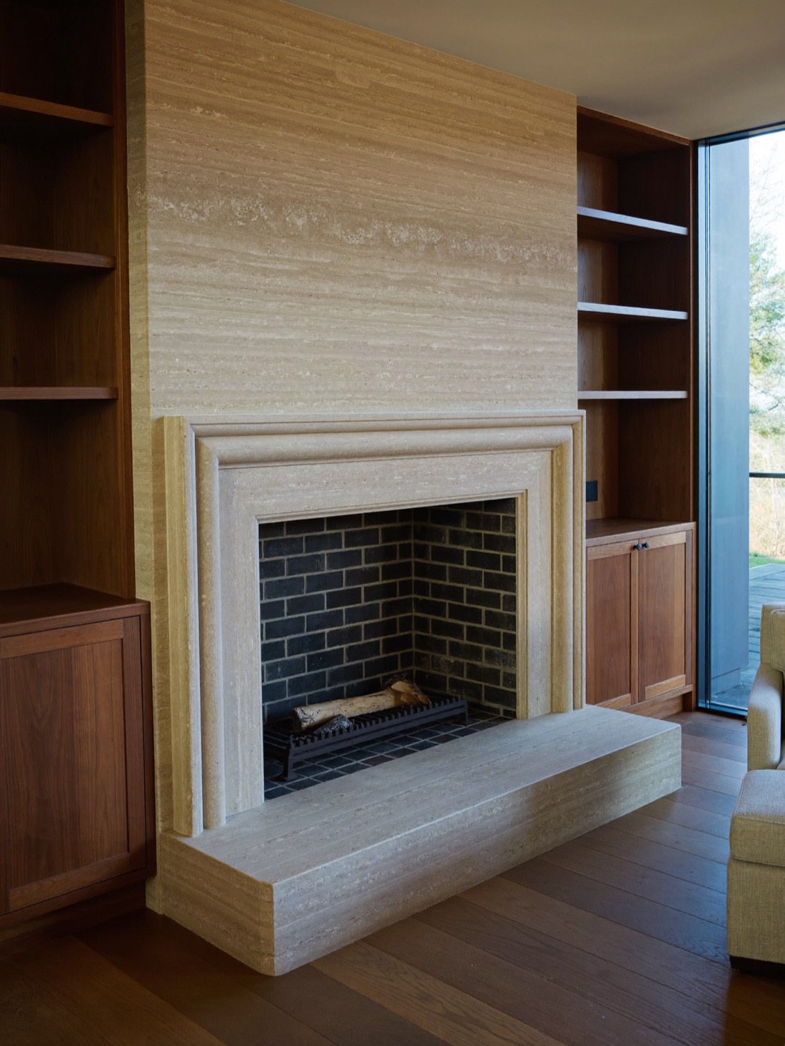Living room fireplace with a pale banded stone surround and dark brick firebox, flanked by built-in dark wood shelves and cabinets.